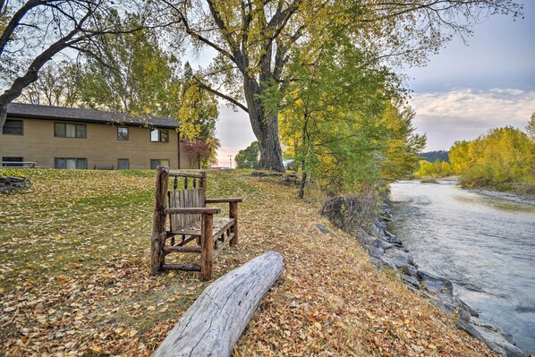 A wooden bench and a log by a riverbank, with a building in the background.