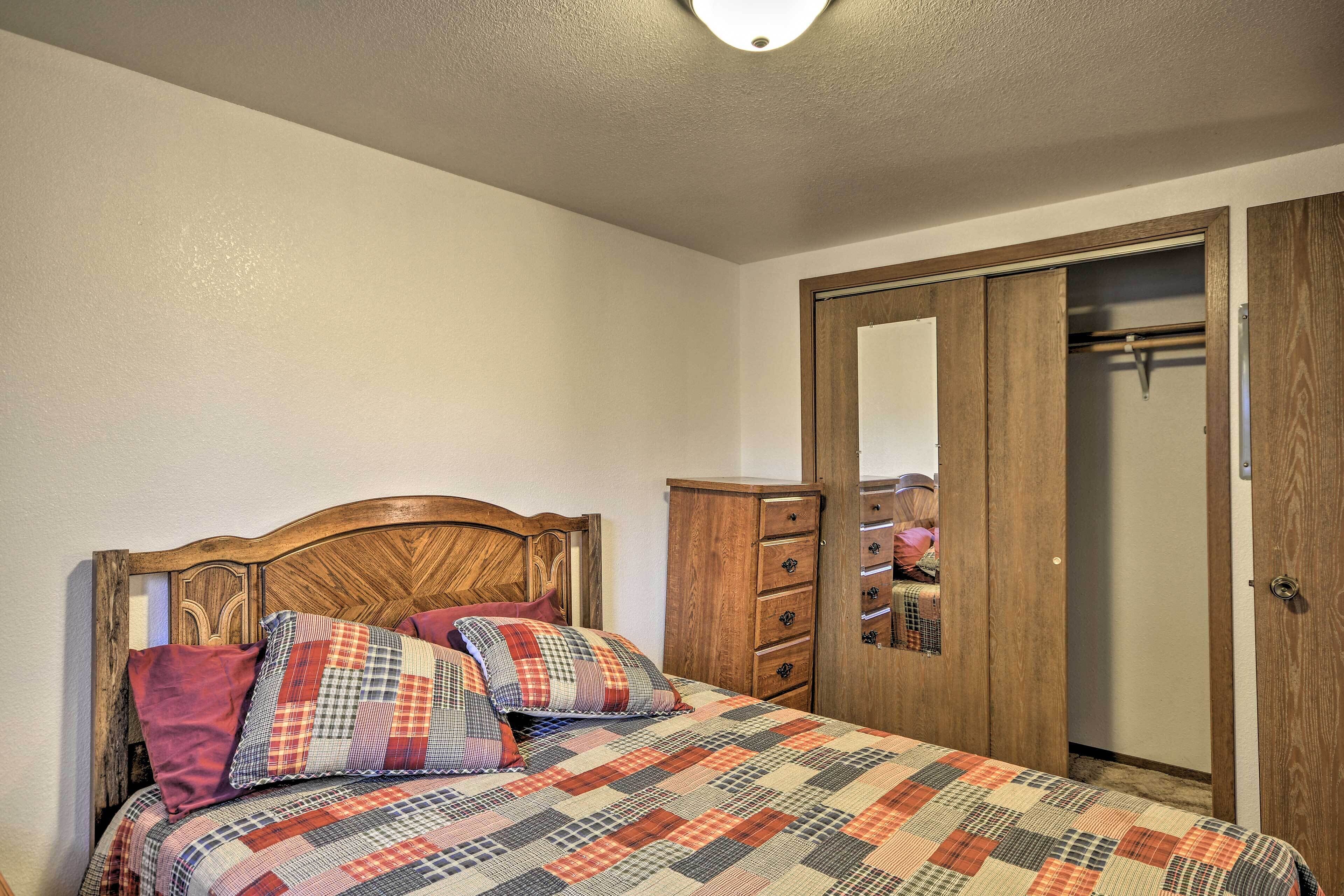 A bedroom with a wooden bed, a quilt, a wooden wardrobe, and a mirror.