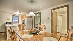 A dining area with a wooden table, four chairs, a central floral arrangement, and a kitchen in the background. - Charming Columbus Apt Along Yellowstone River (Columbus)