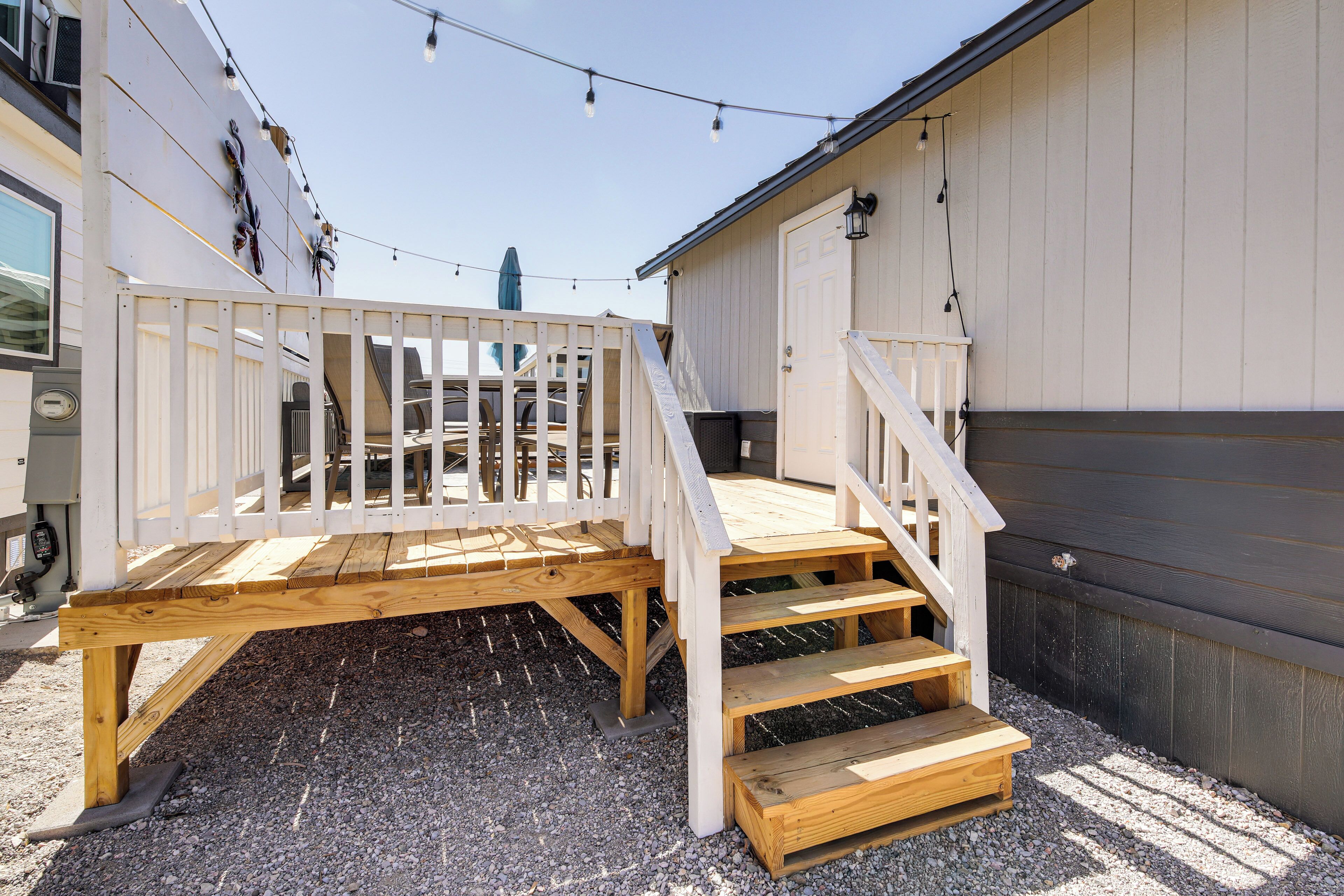 Una terraza de madera con barandilla blanca, escalones de madera y suelo de grava.