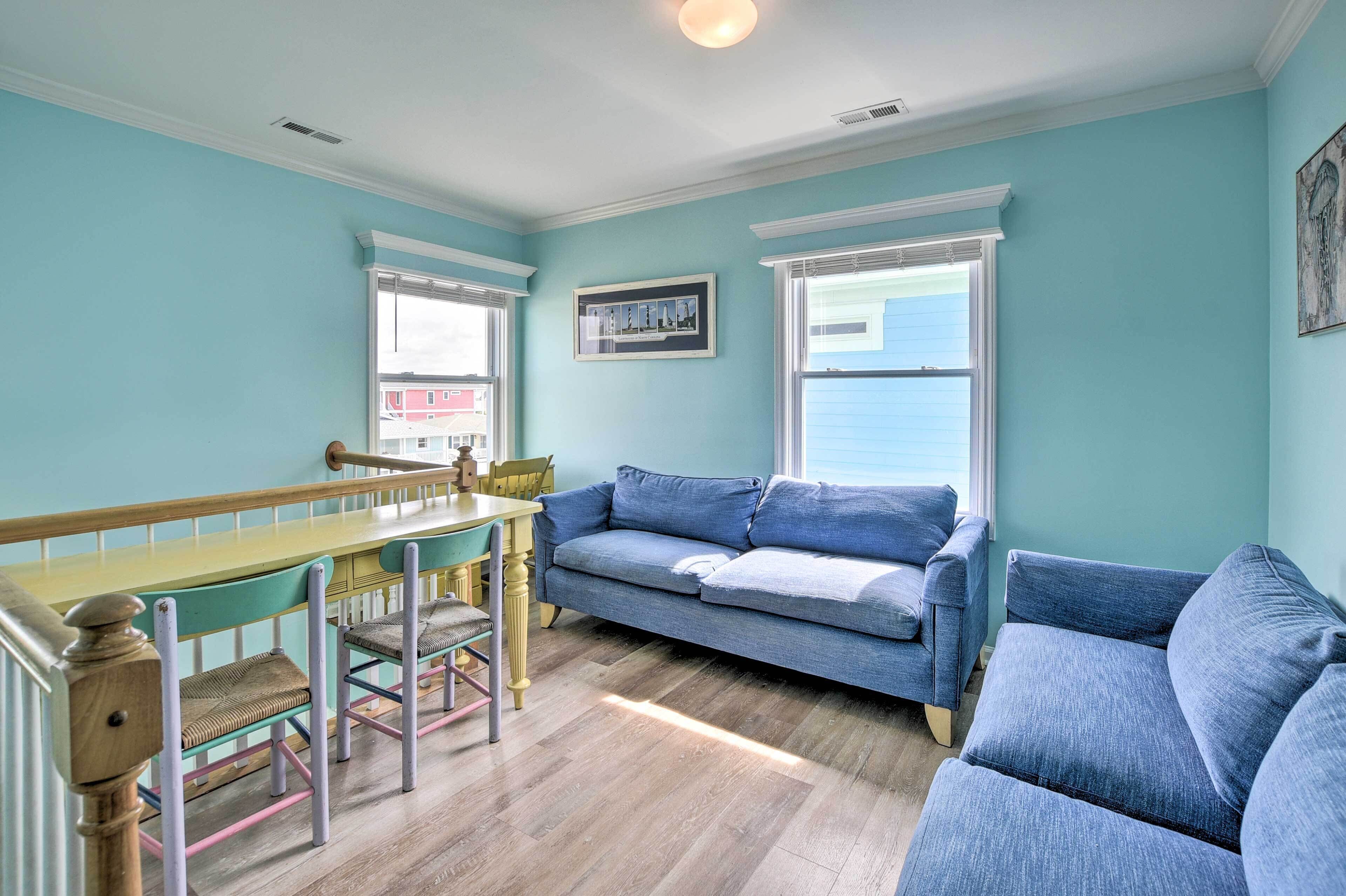 A room with a dining table, two blue sofas, and a window with a view of a building.