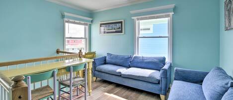 A room with a dining table, two blue sofas, and a window with a view of a building.