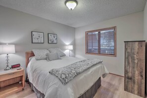 Ein Schlafzimmer mit einem Bett, Nachttischlampen, einem Beistelltisch und einem Fenster mit Jalousien.