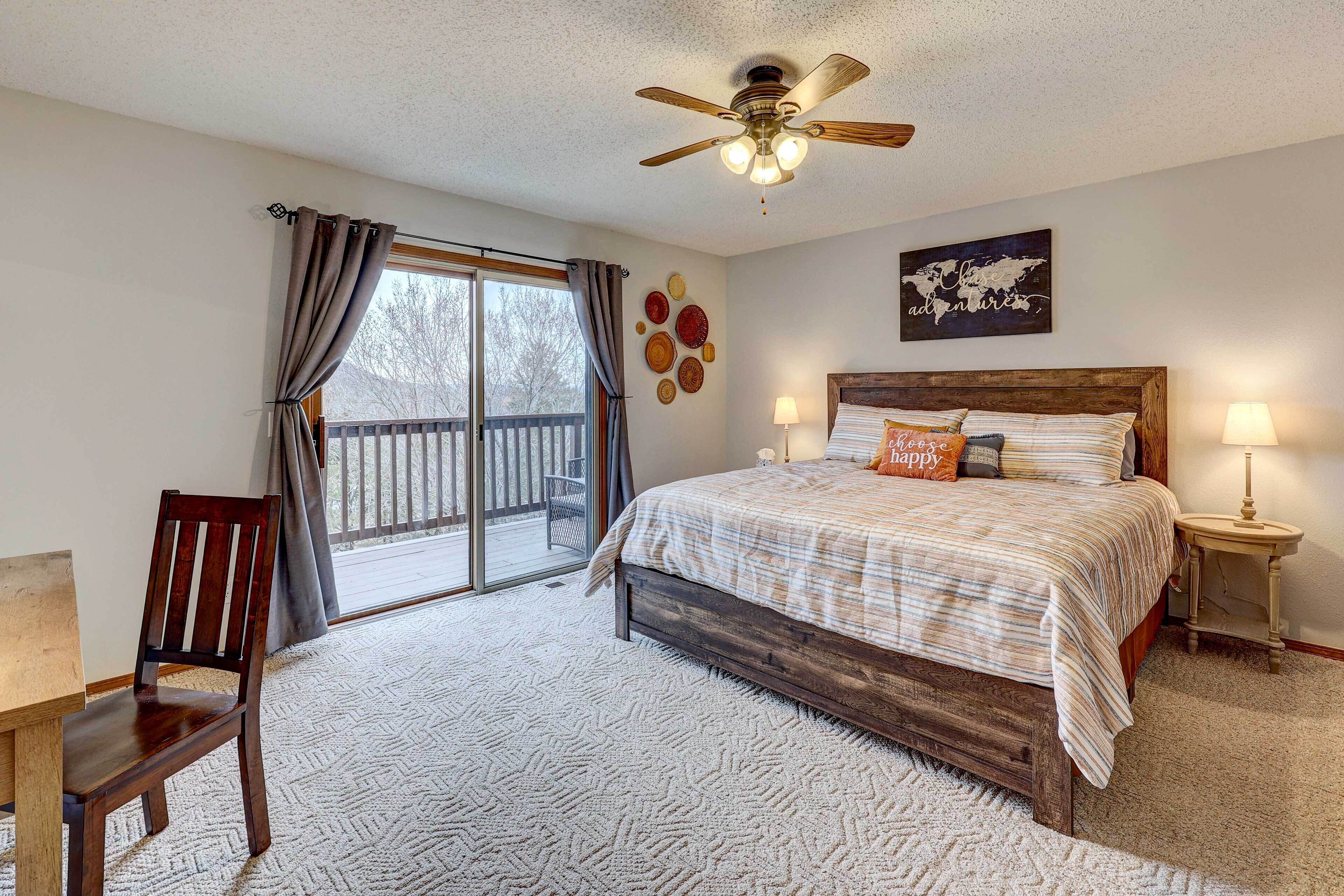 A bedroom with a bed, a chair, a ceiling fan, a window with curtains, and a view of the outdoors.