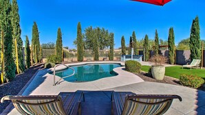 Un patio trasero con piscina, sillas de descanso y un paraguas rojo.