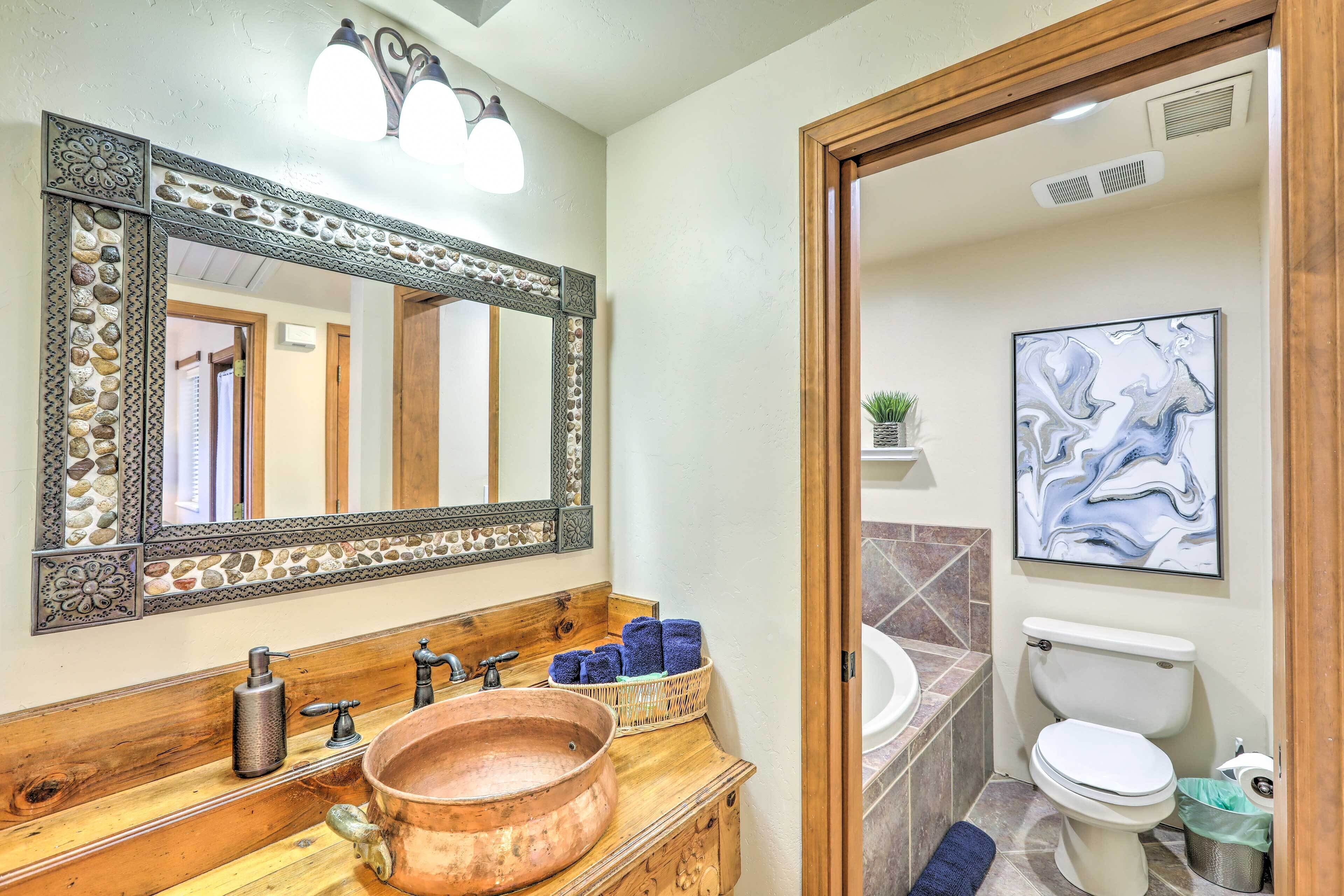 A bathroom with a copper sink, wooden vanity, decorative mirror, and a modern abstract painting.