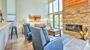 A spacious living area with a stone fireplace, leather seating, and large windows. - Mountain-view Deck: Bright Sedona Home (Sedona)