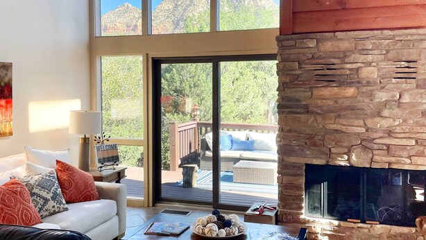 A cozy living room with a fireplace, large windows, and a deck with outdoor furniture. - Mountain-view Deck: Bright Sedona Home (Sedona)