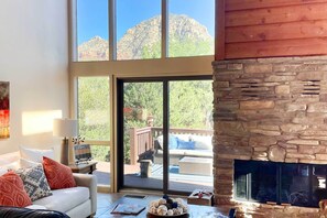 A cozy living room with a fireplace, large windows, and a deck with outdoor furniture. - Mountain-view Deck: Bright Sedona Home (Sedona)