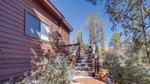 A wooden cabin with a staircase leading to a deck, surrounded by trees and shrubs. - Mountain-view Deck: Bright Sedona Home (Sedona)