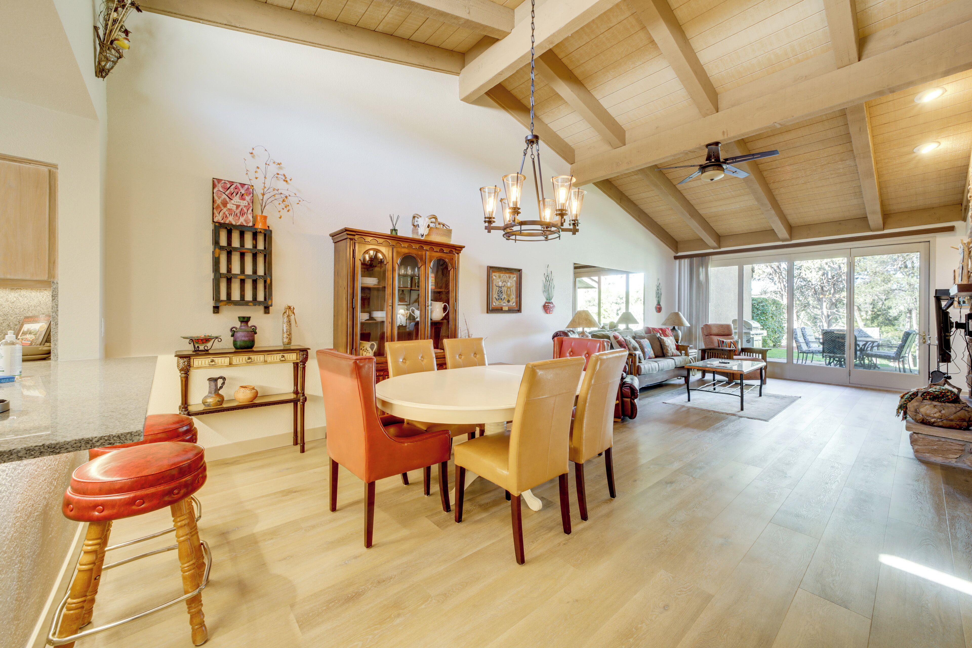 A spacious living area with a high ceiling, a dining table surrounded by chairs, a wooden cabinet, and a large window providing a view of the outdoors.
