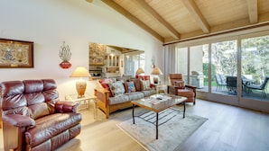 A spacious living room with a leather armchair, a sofa, and a coffee table. There is a stone wall and a large window providing a view of the outdoors. - Sedona Home w/ Golf Course View & Pool Access! (Sedona)