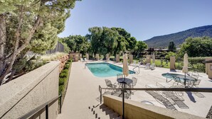 A pool area with lounge chairs and a table, surrounded by trees and a mountain in the background. - Sedona Home w/ Golf Course View & Pool Access! (Sedona)