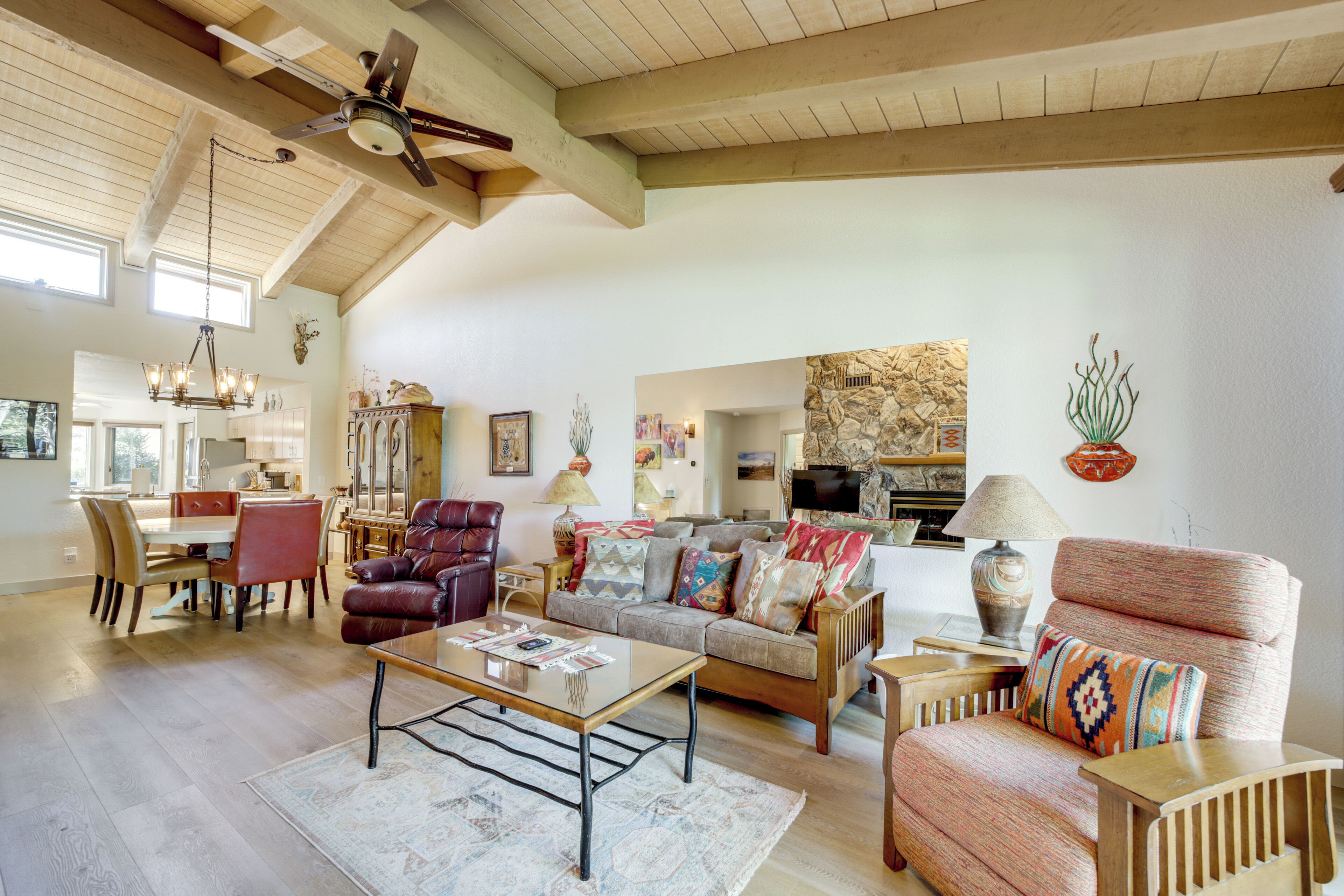 A spacious living room with a high ceiling, wooden beams, a dining area, and a kitchen in the background.