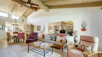 A spacious living room with a high ceiling, wooden beams, a dining area, and a kitchen in the background.