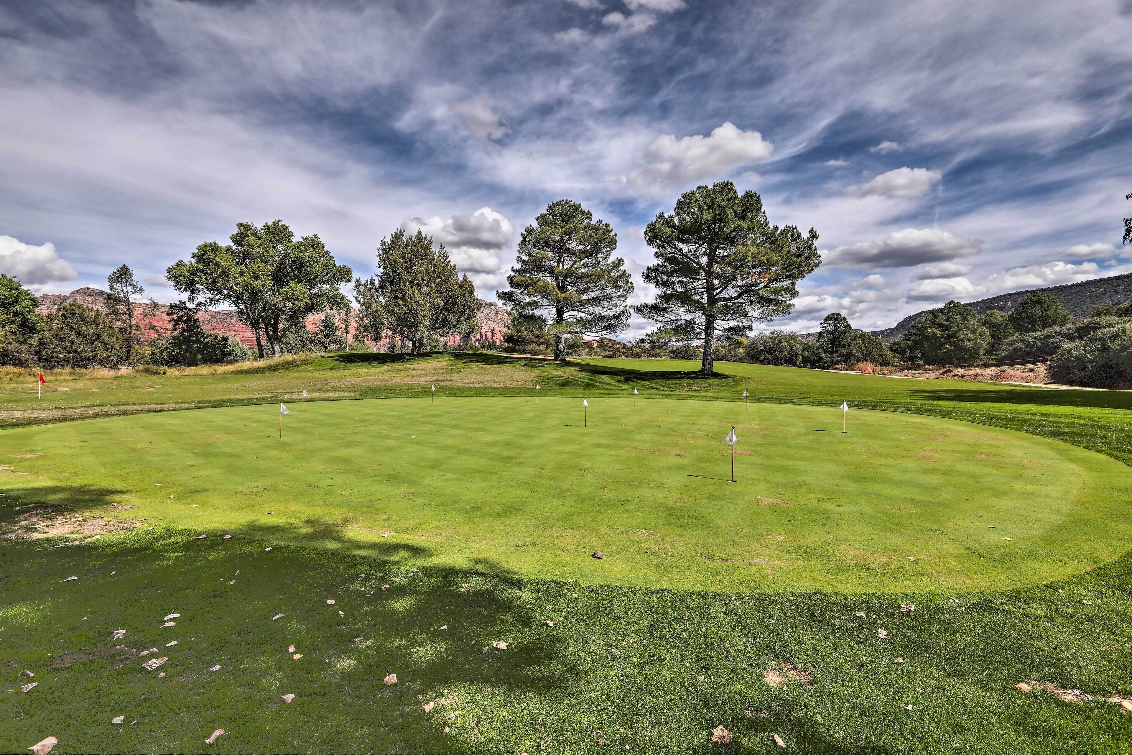 Un campo de golf con un césped bien cuidado, árboles y colinas al fondo.