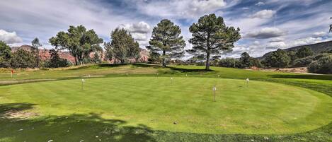 Un campo de golf con un césped bien cuidado, árboles y colinas al fondo.