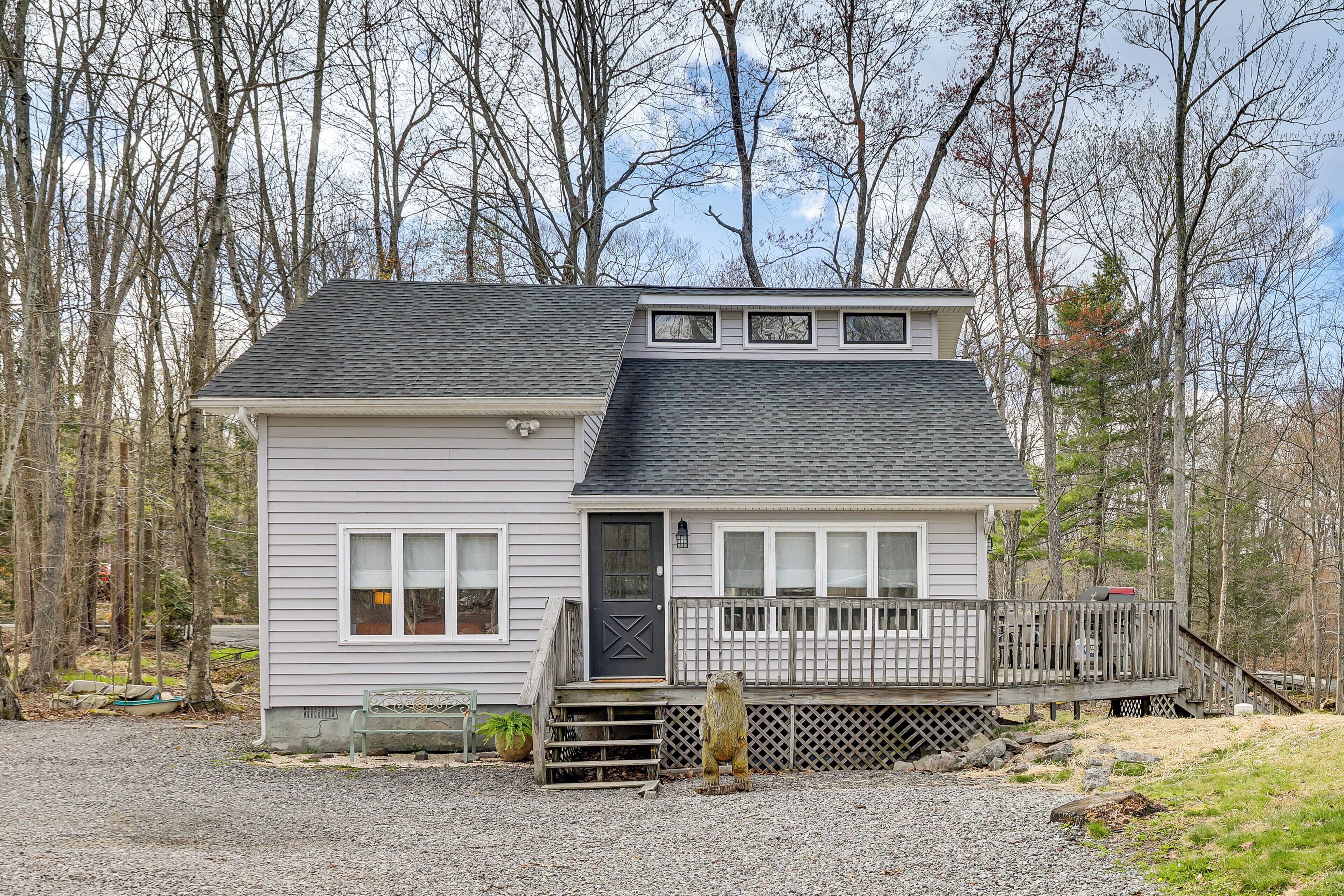 A two-story house with a front porch, a small deck, and a gravel driveway.