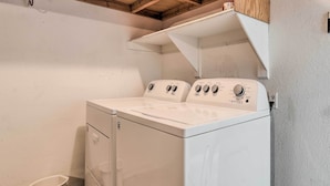 A laundry room with a front-loading washer and dryer, a small trash bin, and a wooden shelf above the dryer. - 2 Mi to Sports Complex: Peoria Home w/ Patio! (Peoria)