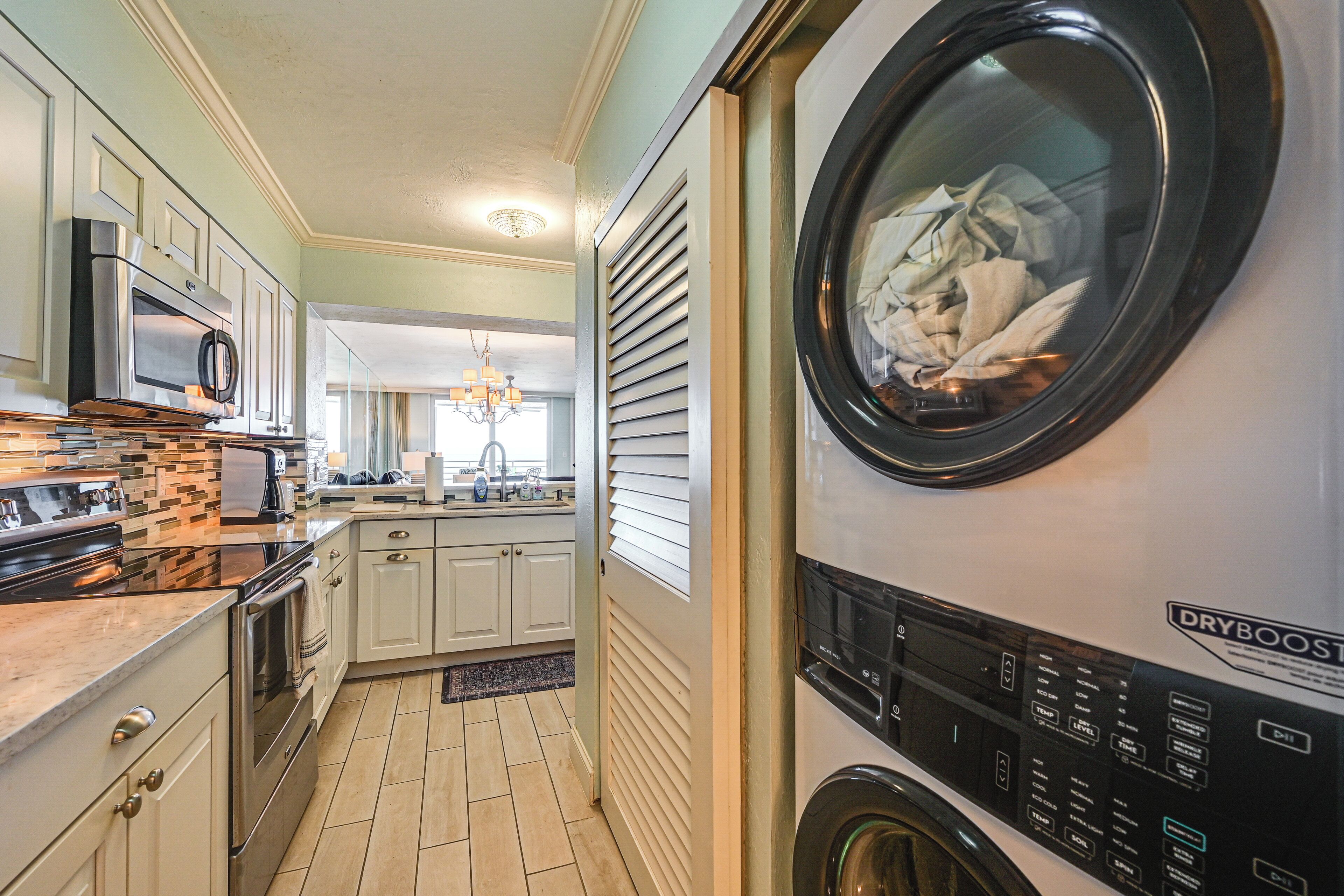 A laundry room with a front-loading washer and dryer, a kitchen with modern appliances, and a hallway leading to a dining area.