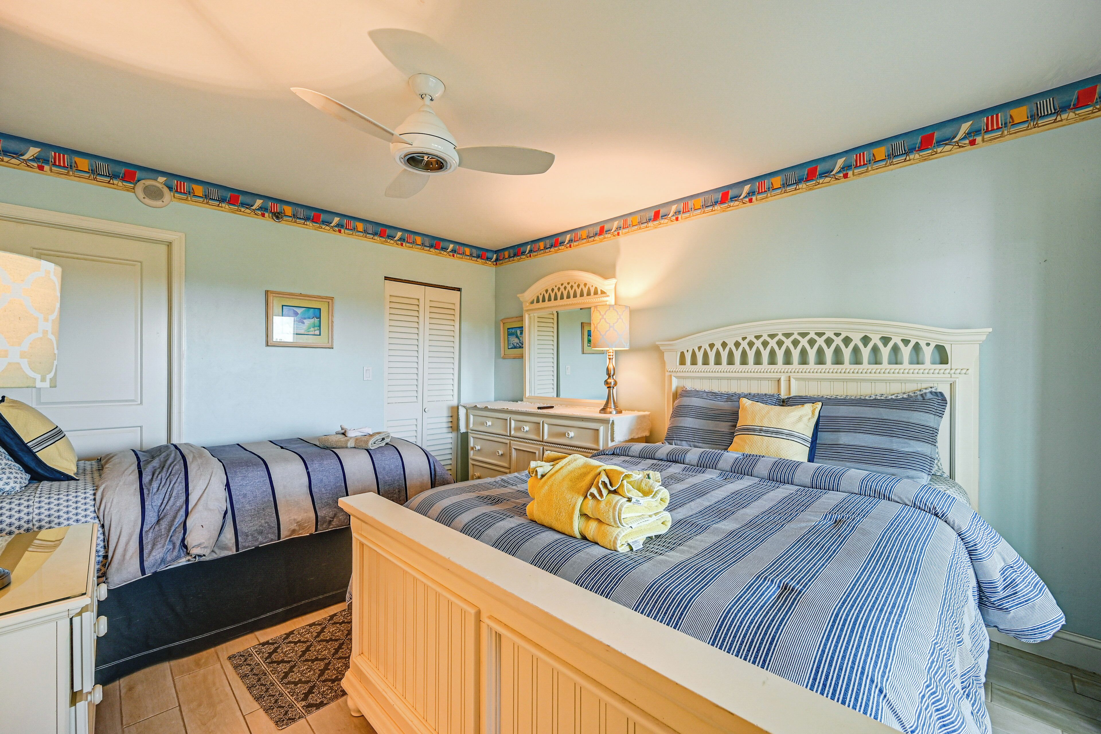 A bedroom with a bed, a dresser, a nightstand, a ceiling fan, and a window.
