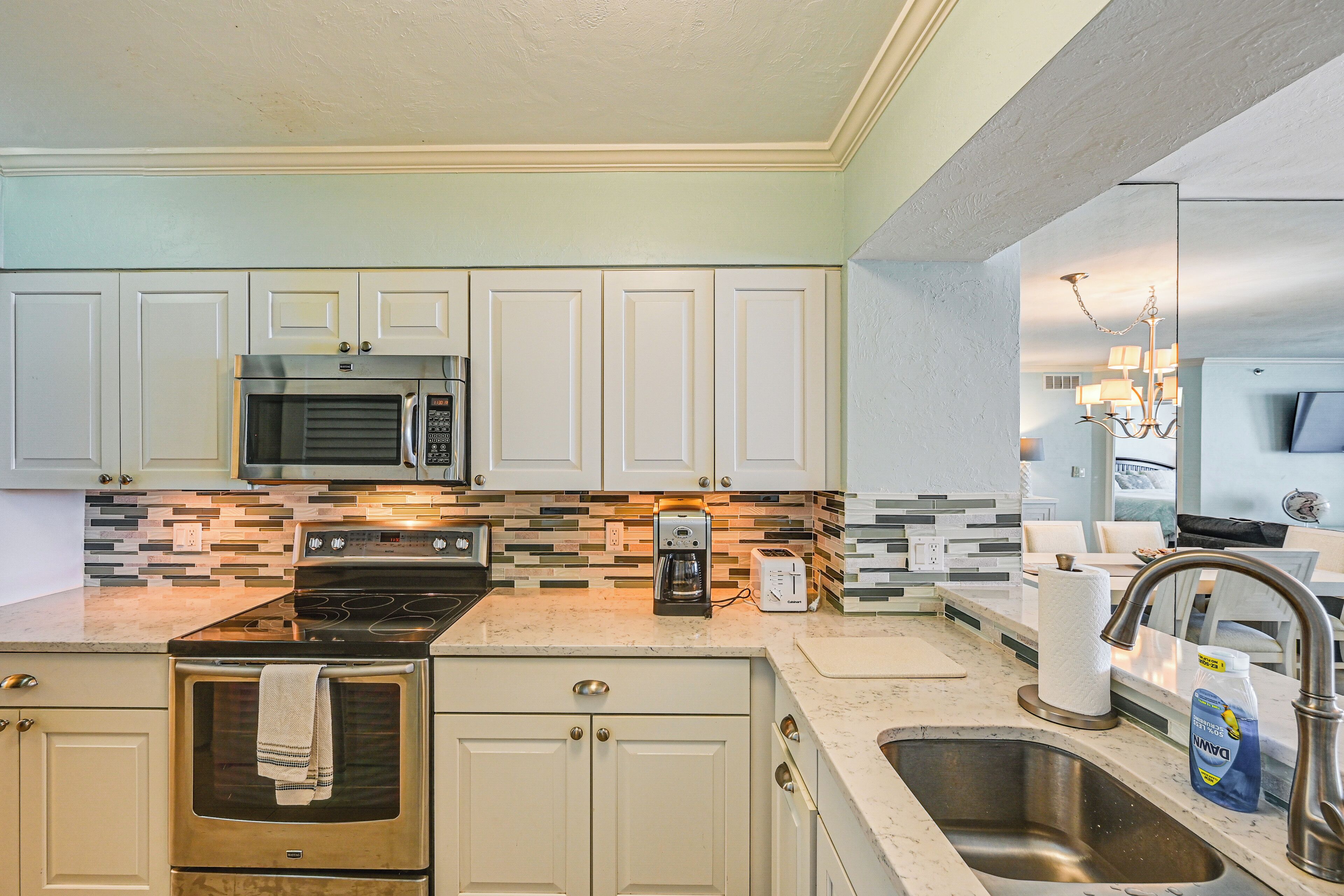 A kitchen with white cabinets, a stainless steel microwave, a stove, and a sink.