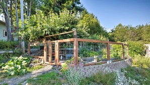 A wooden structure with a glass enclosure, surrounded by a garden with various plants and a stone wall. - Quaint Riverside Reprieve w/ Kayaks + Floats! (Brookings)