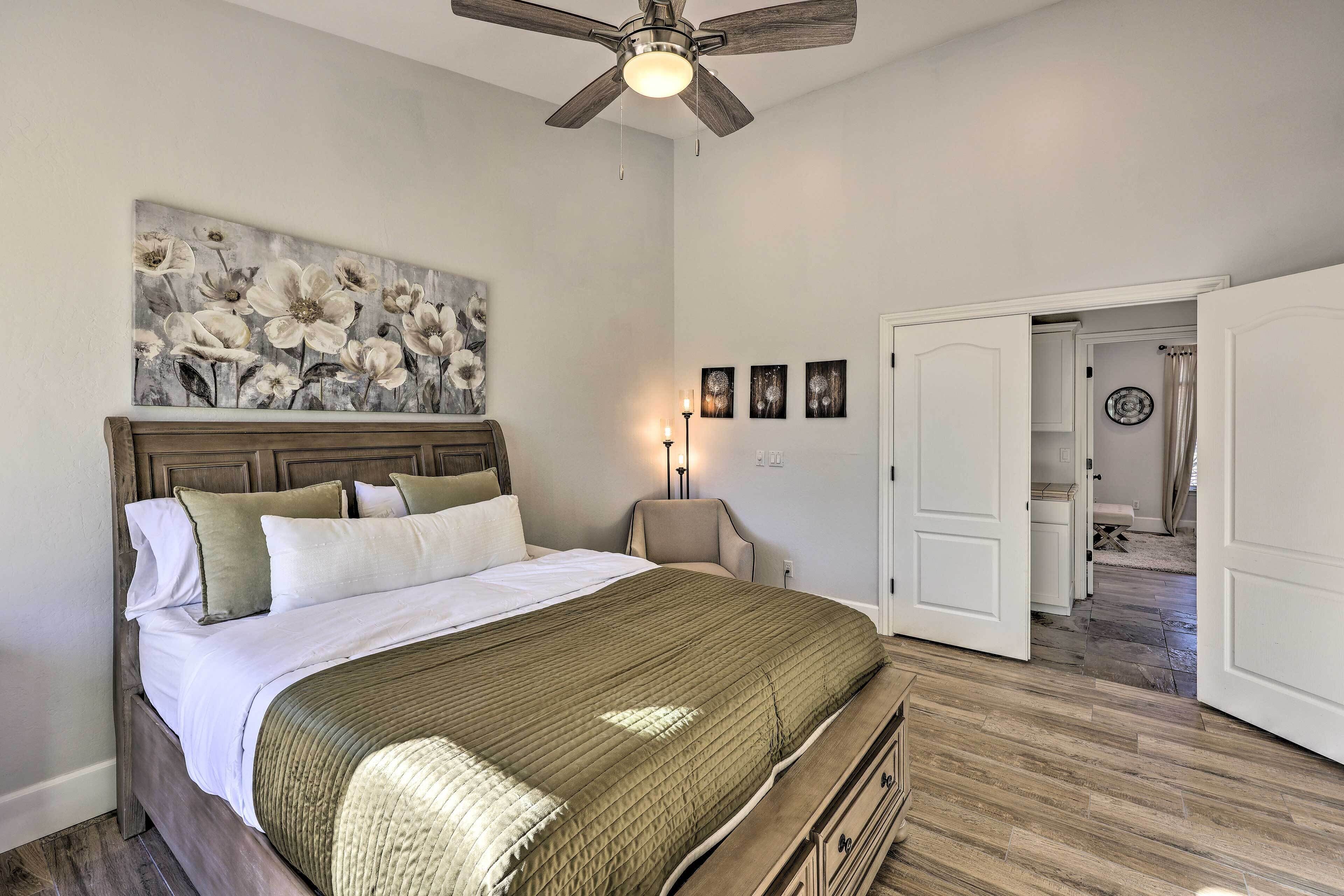 Un dormitorio con cama, ventilador de techo, una obra de arte en la pared y una puerta que da a otra habitación.