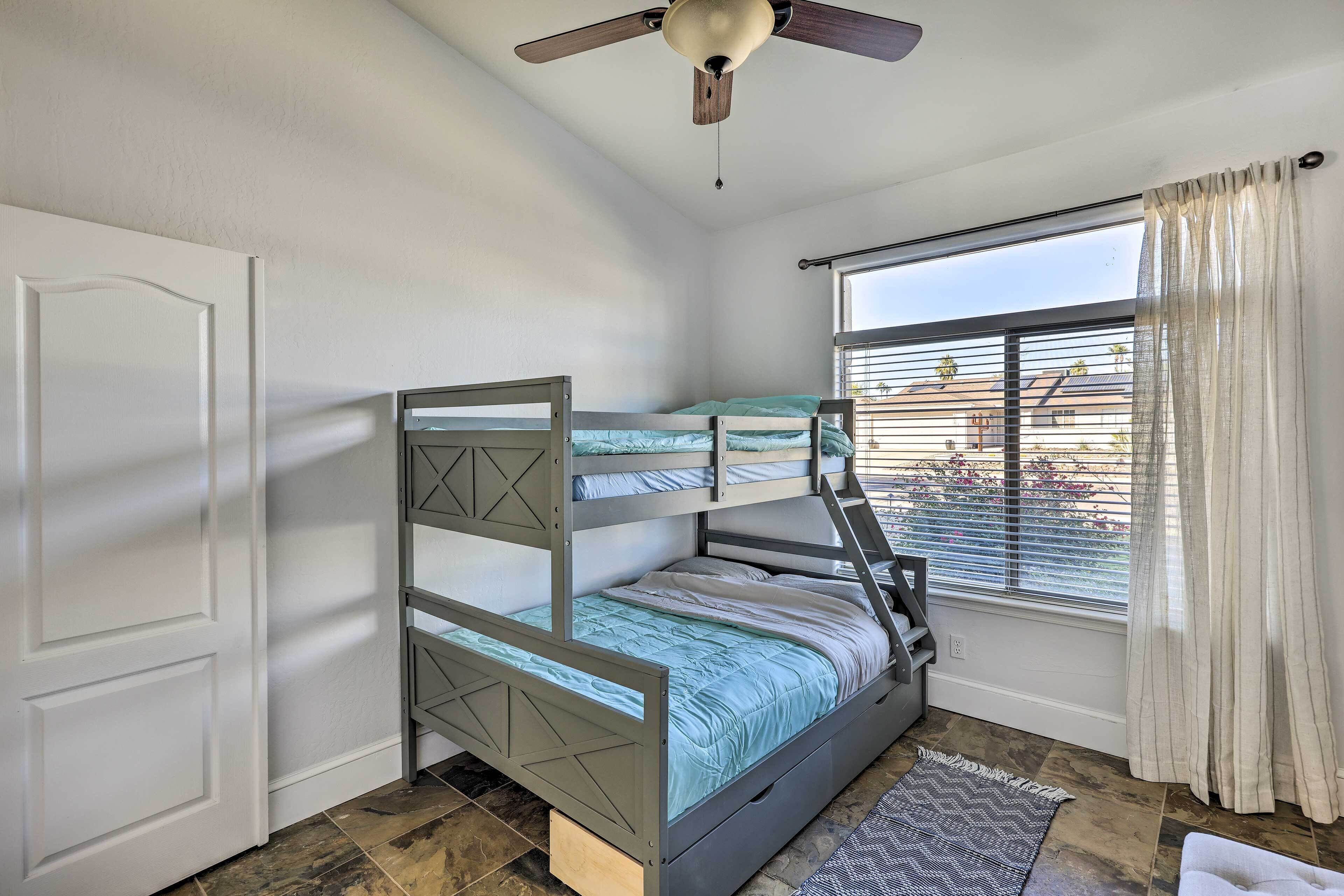 A bunk bed room with a ceiling fan, a window with curtains, and a door.