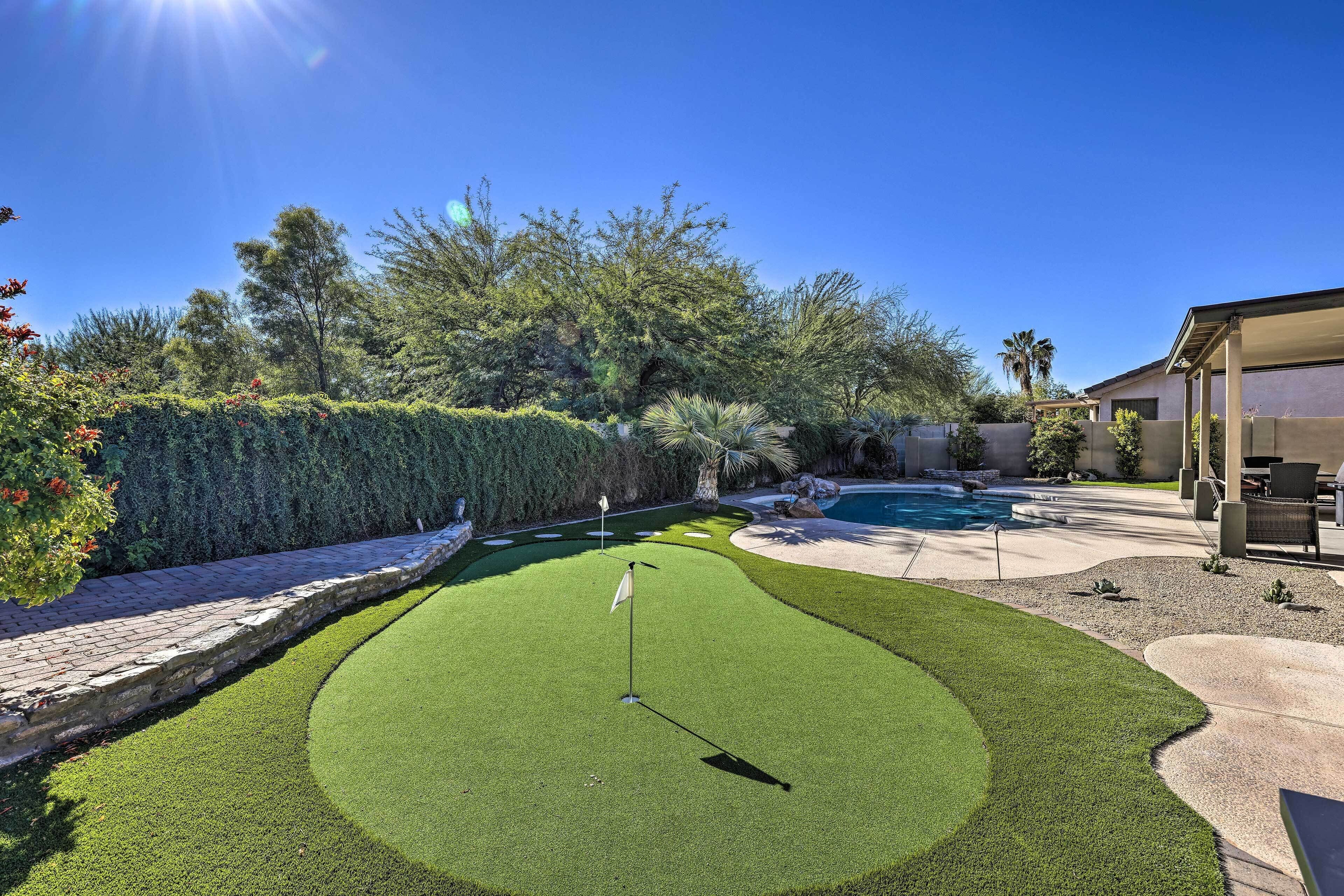 A well-maintained backyard with a putting green, a swimming pool, and a covered patio area.