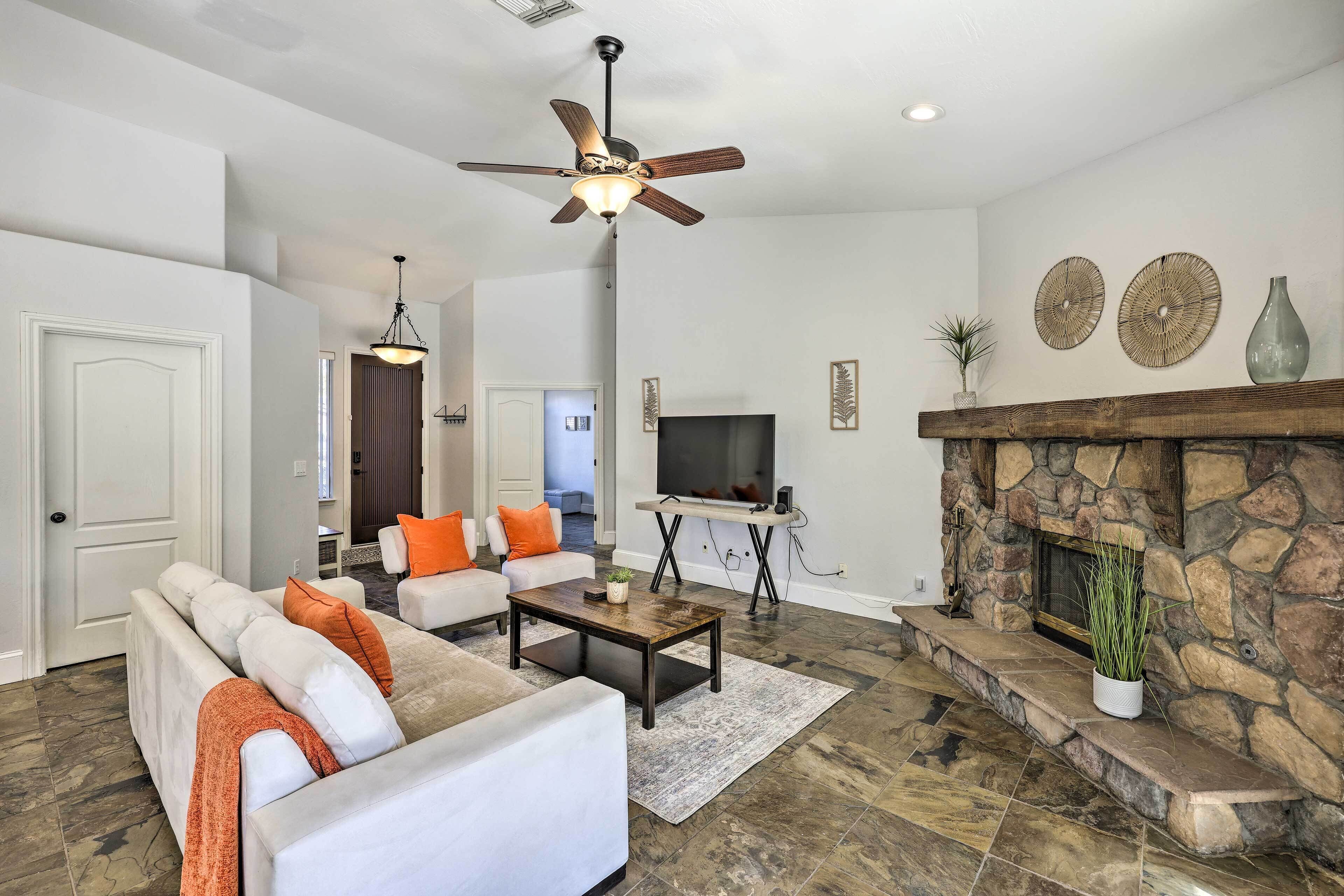 A living room with a stone fireplace, a ceiling fan, and a television.