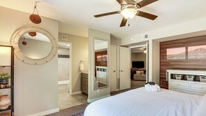Une chambre à coucher comprenant un lit, un ventilateur de plafond, un miroir rond, une commode et une armoire.