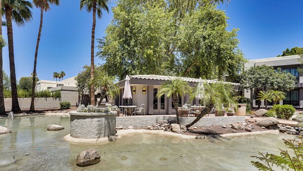 Un espace extérieur paisible avec une piscine, des palmiers et un petit bâtiment doté d’un espace de détente en plein air.