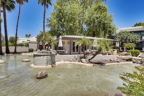 Un espacio exterior tranquilo con piscina, palmeras y un pequeño edificio con mesas al aire libre.