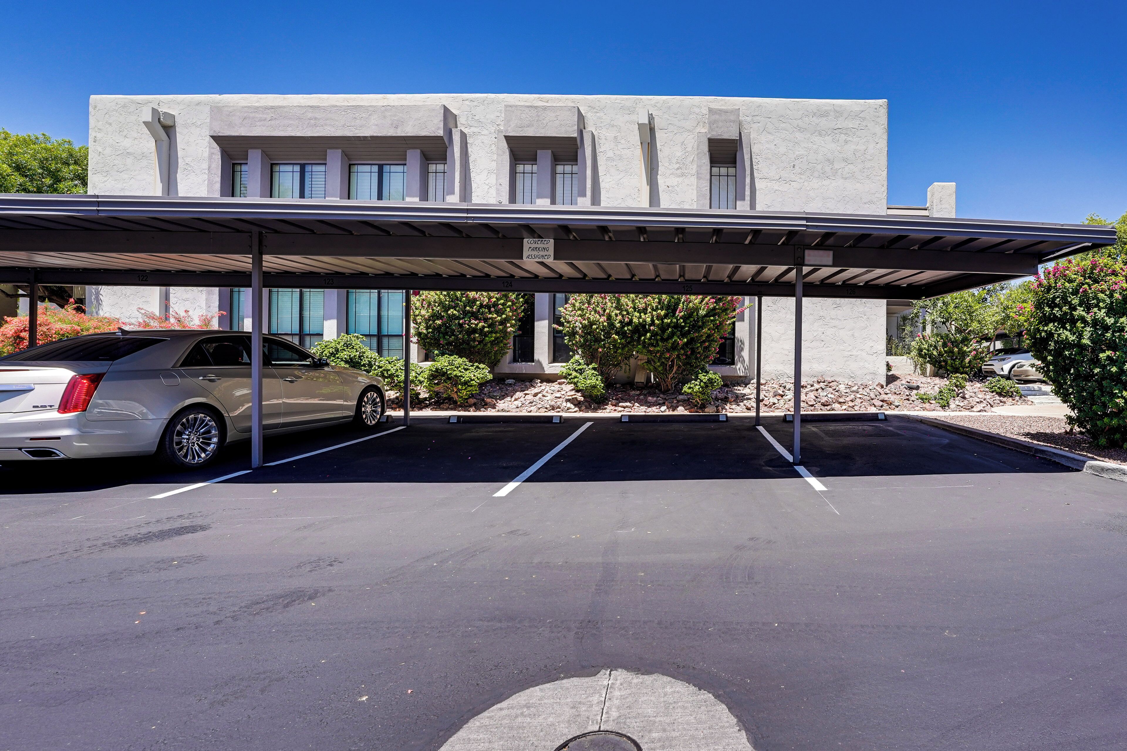 A parking area with a covered structure, a building with large windows, and a parked car.