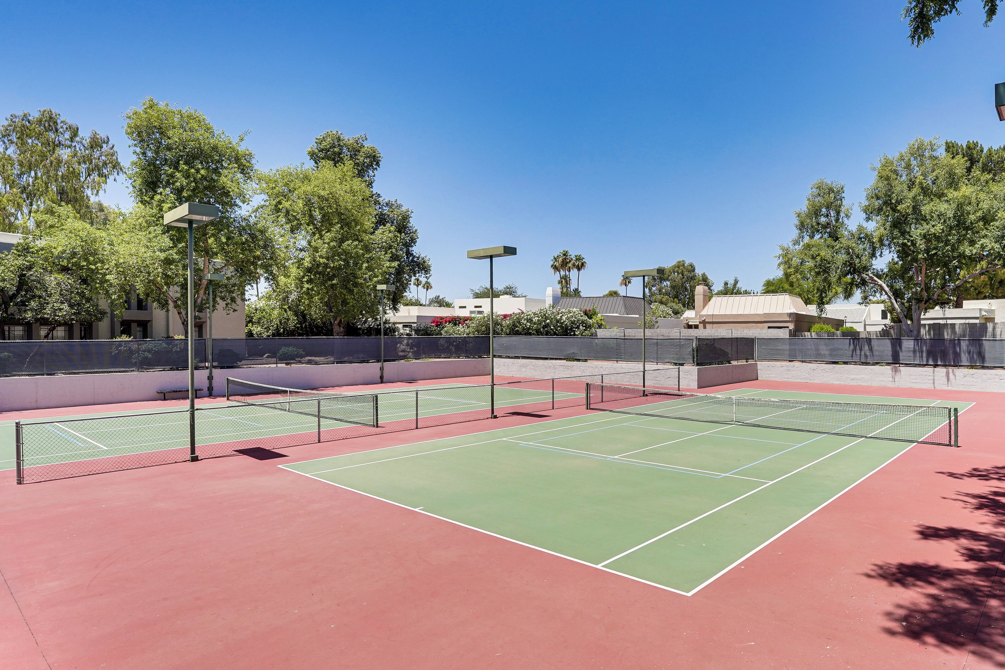 A tennis court with a net, surrounded by trees and buildings.