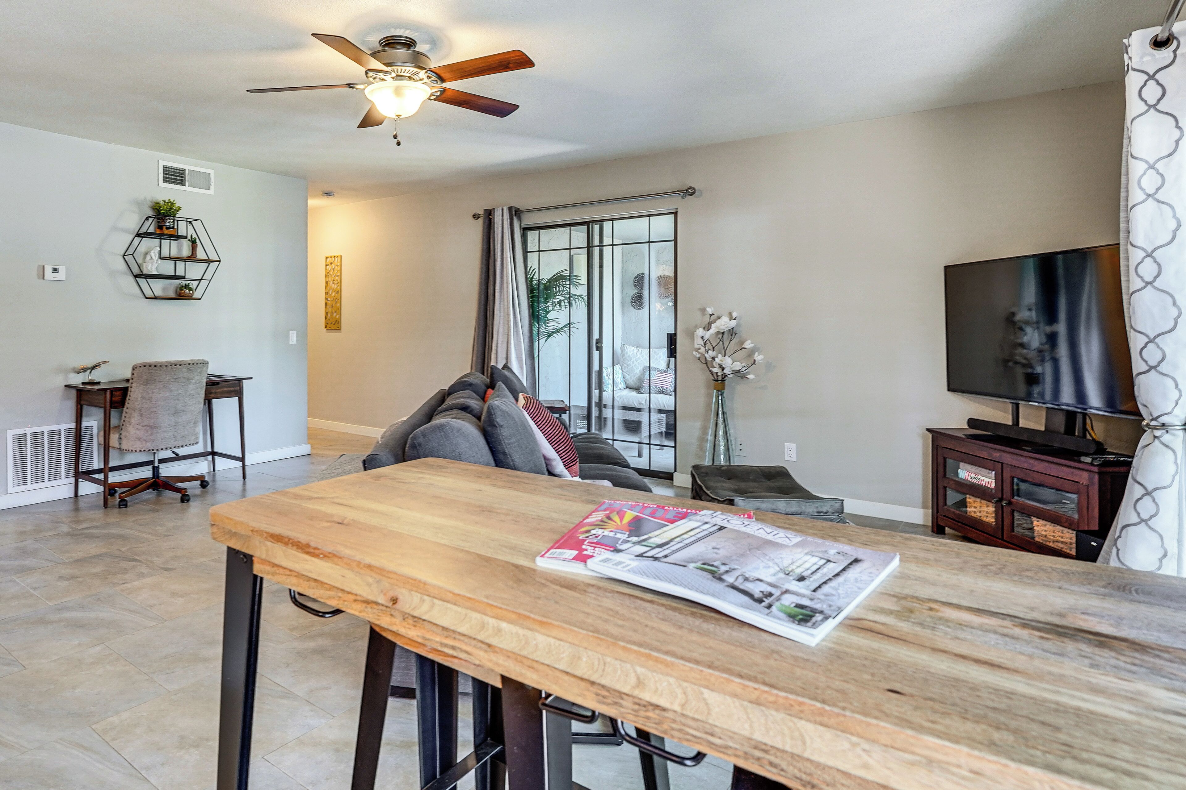 Una sala moderna con una mesa de comedor de madera, un sofá, un televisor y un ventilador de techo.