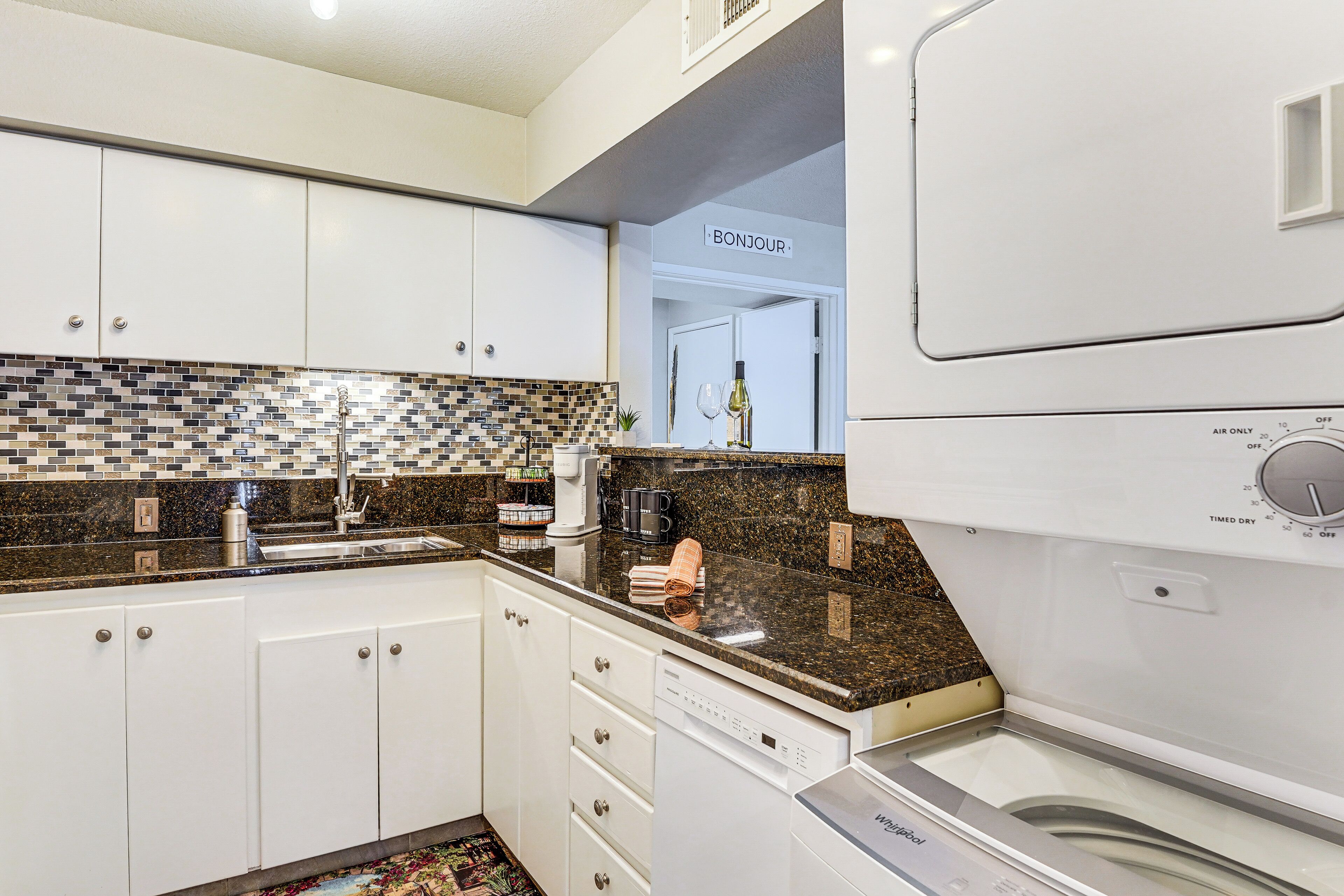 A modern kitchen with white cabinets, a tiled backsplash, and a built-in dishwasher.