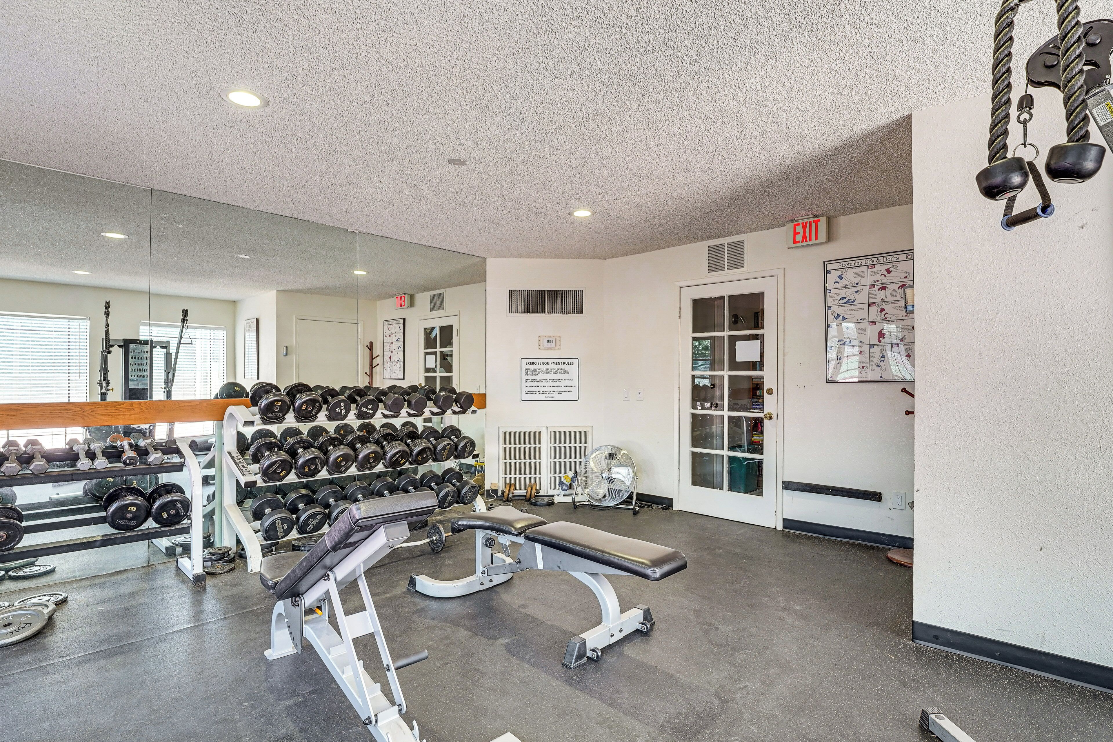 A gym with weightlifting equipment, a bench, and a wall-mounted mirror.