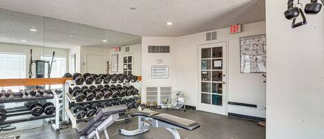A gym with weightlifting equipment, a bench, and a wall-mounted mirror.