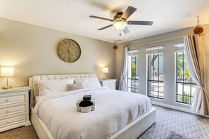 Un dormitorio con cama, ventilador de techo, reloj y ventana con cortinas.