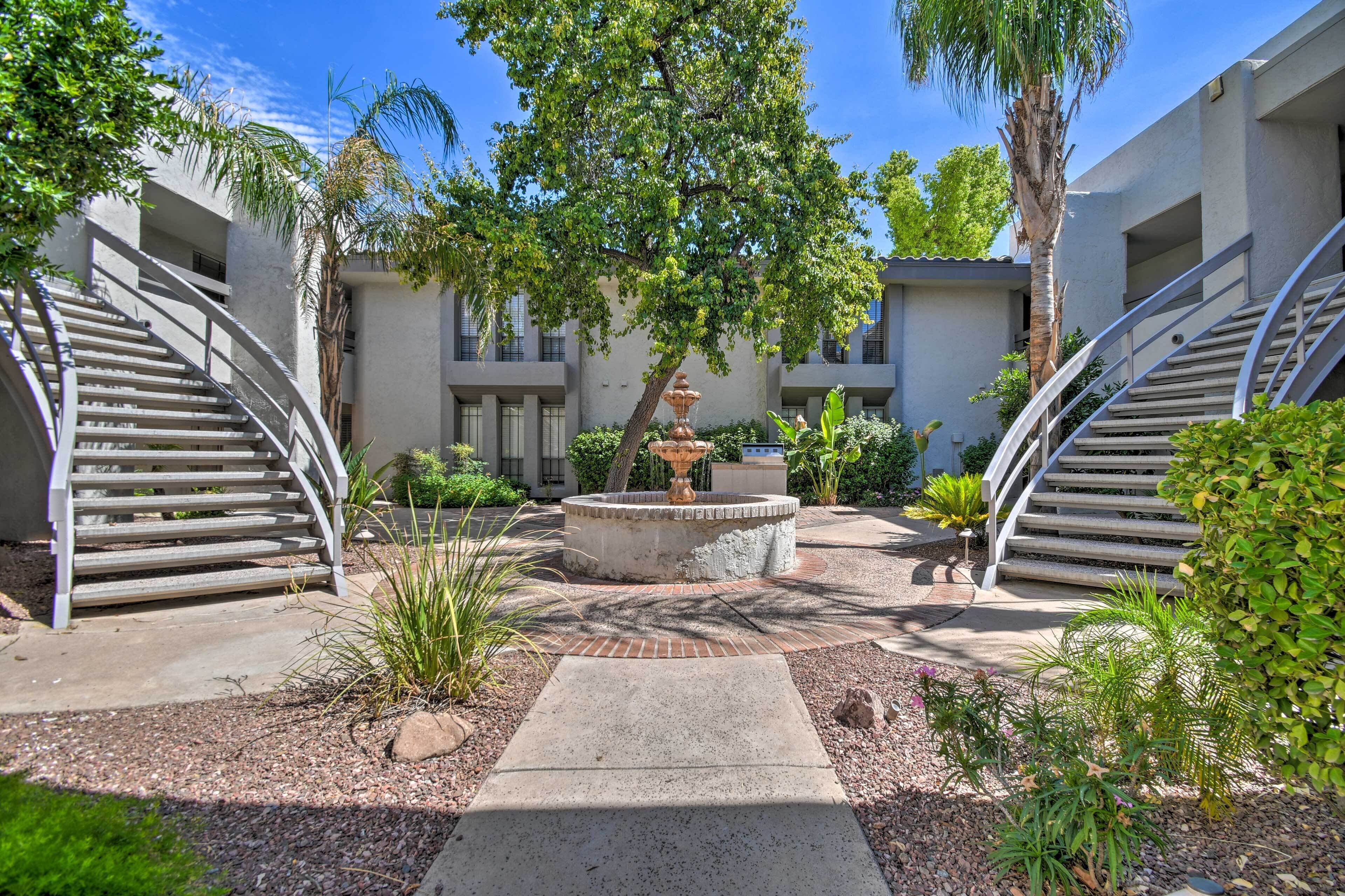 A courtyard with a central fountain, surrounded by palm trees and a building with a modern design.