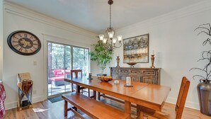A dining area with a wooden table, benches, and a chandelier. There is a clock on the wall and a painting above the cabinets. - Flagstaff Hideaway: Private Hot Tub, 4 Mi to Dtwn! (Flagstaff)