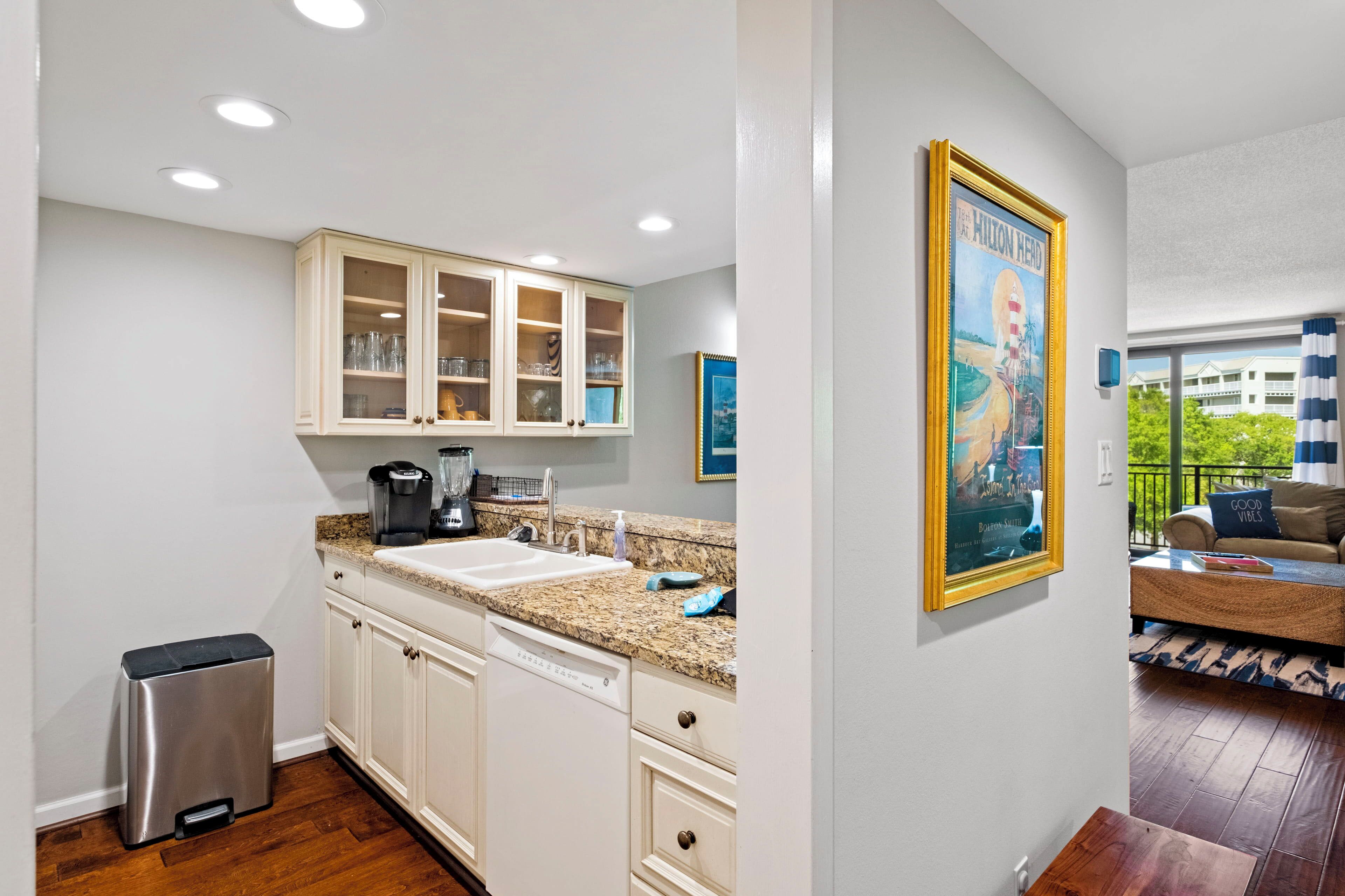 A kitchen with white cabinets, a granite countertop, and a stainless steel trash can.
