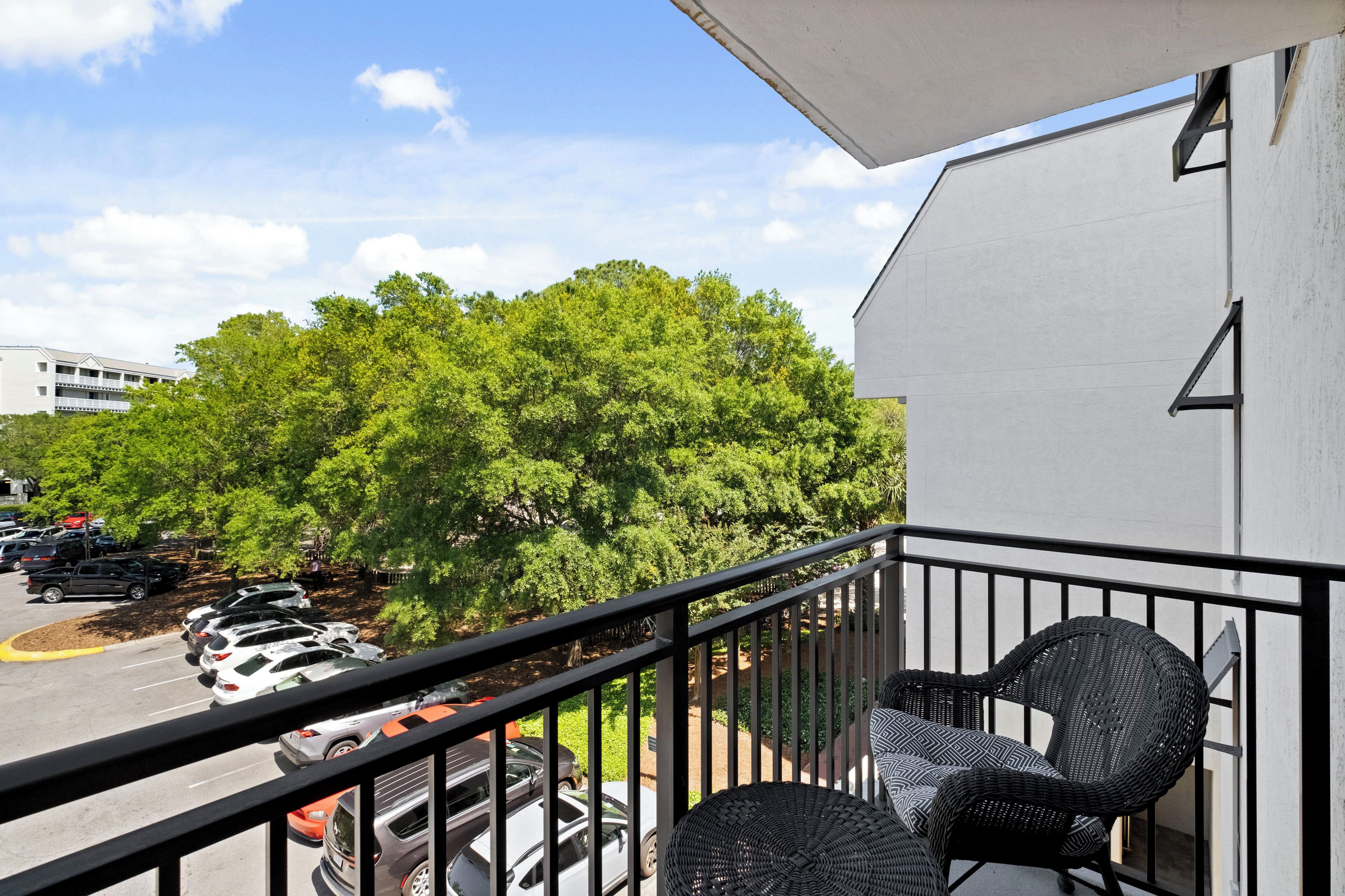 A balcony with wicker furniture, a parking lot, and a building with a white exterior.