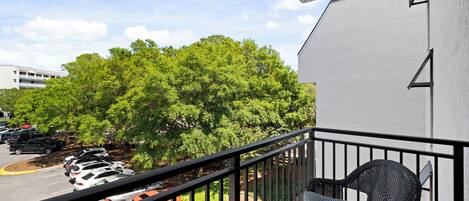 A balcony with wicker furniture, a parking lot, and a building with a white exterior.