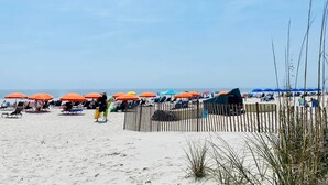 Ein Strand mit Reihen von Liegestühlen und Sonnenschirmen, einer Holzlattenveranda und einem klaren Himmel.