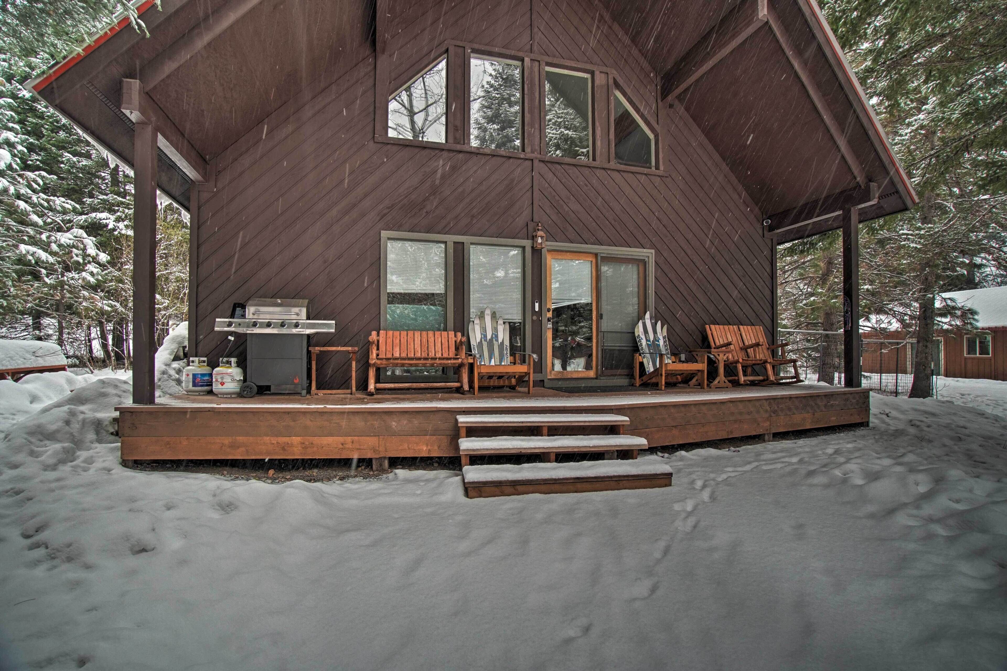 A wooden cabin with a deck, outdoor seating, and a grill.