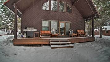 A wooden cabin with a deck, outdoor seating, and a grill.
