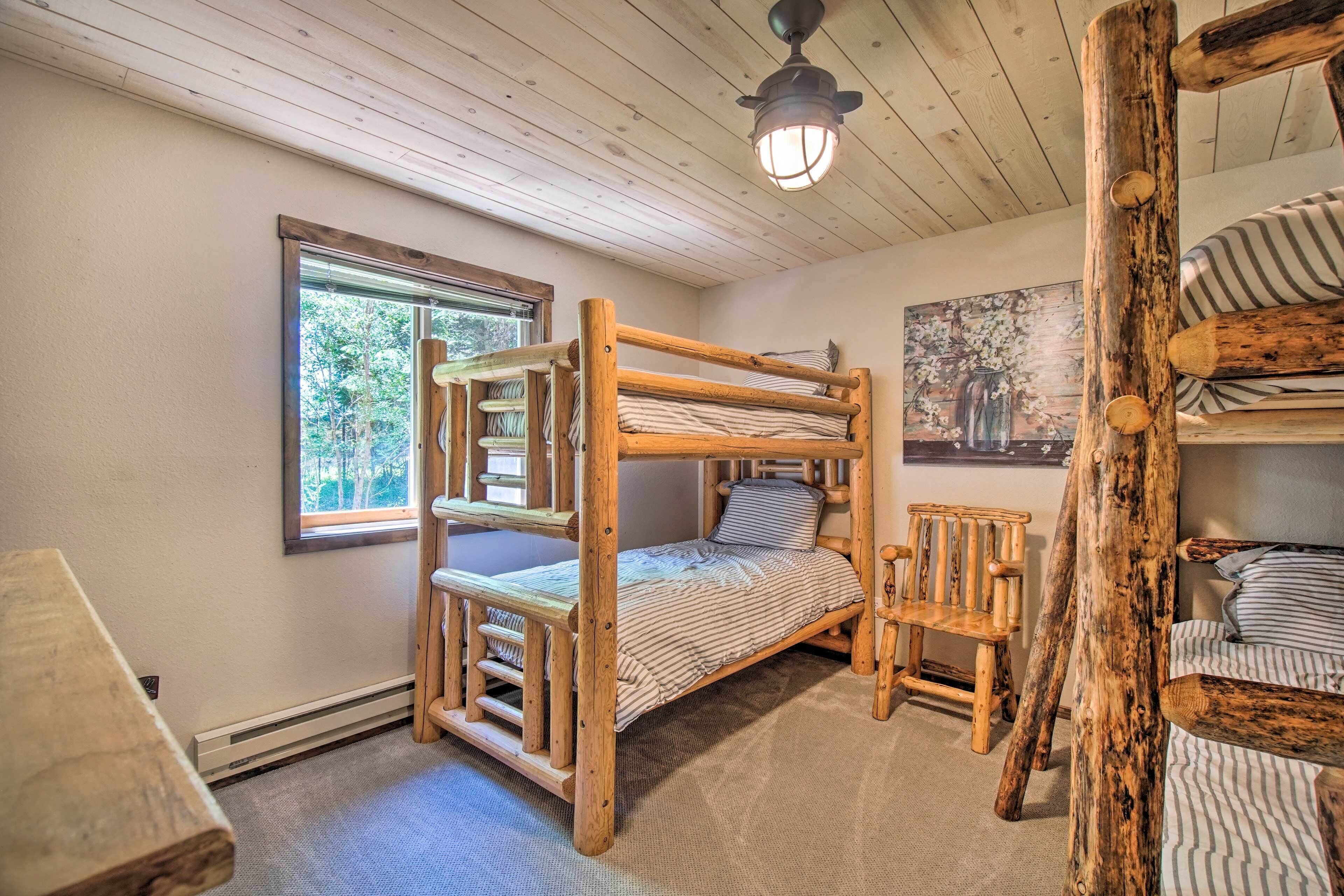 A rustic cabin room with a bunk bed, a wooden chair, a window with a view of trees, and a ceiling fan.
